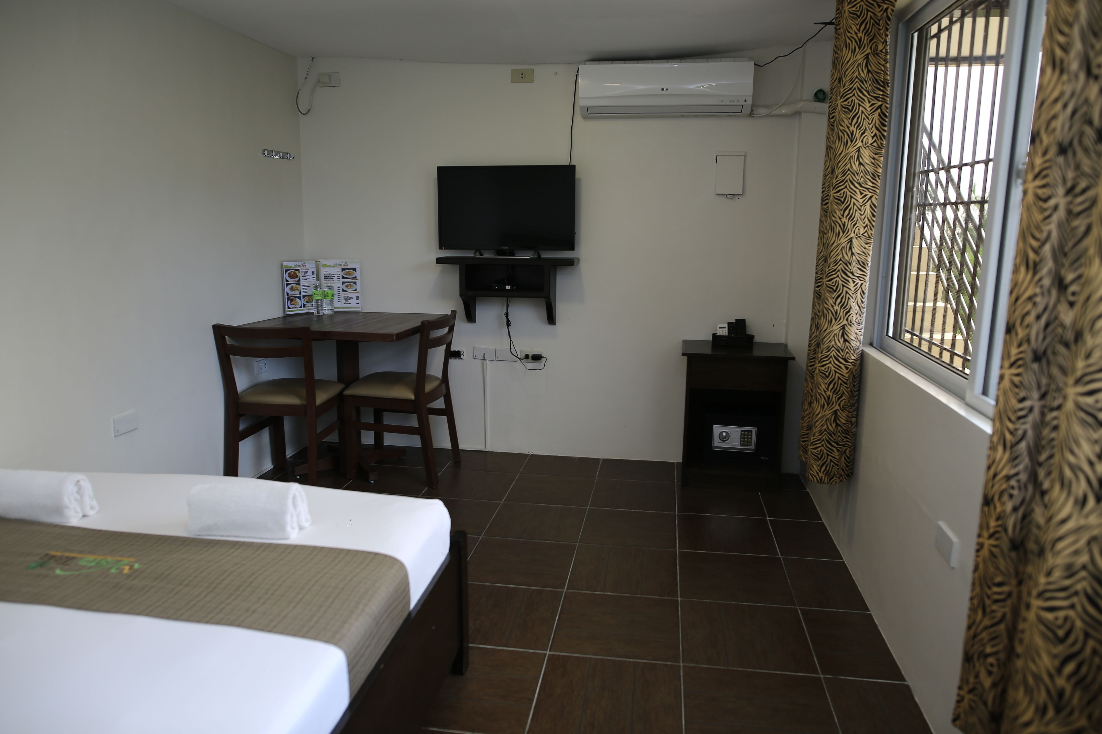 Habitación de hotel con cama, escritorio y silla, televisor y ventana con cortinas estampadas.