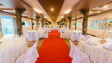 Une salle de banquet avec une allée recouverte d’un tapis rouge, des nappes blanches et des lustres à bougies.