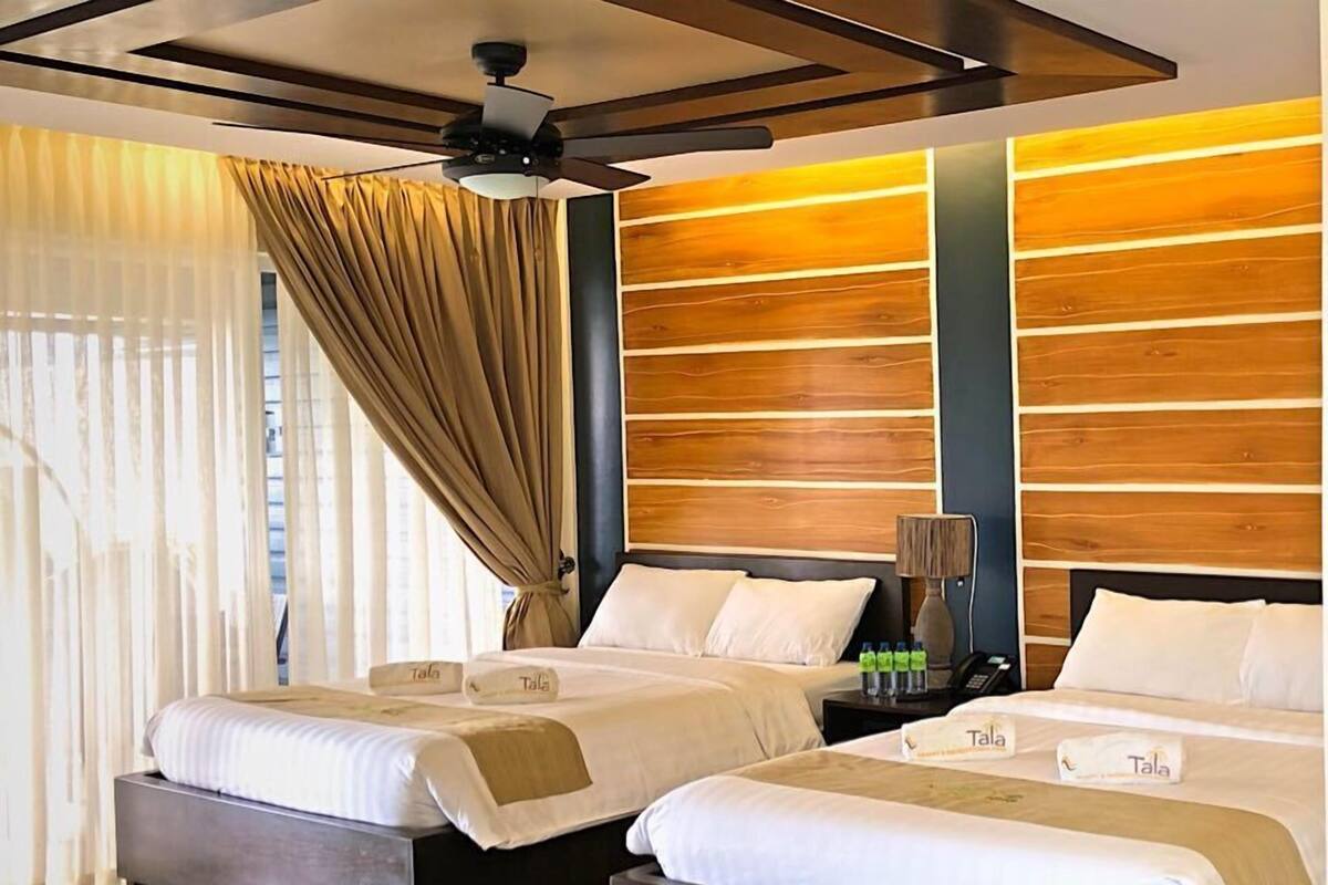 Une chambre d’hôtel avec deux lits, un ventilateur de plafond, un mur décoratif en bois et un sol à motifs.