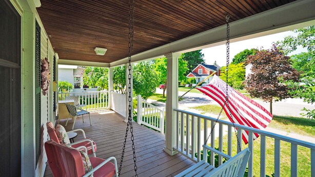 Eine überdachte Veranda mit Schaukel und Blick auf eine Wohnstraße, sowie eine amerikanische Flagge.