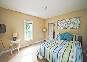 Un dormitorio con cama, una mesita de noche, una lámpara, una ventana y un cuadro en la pared.