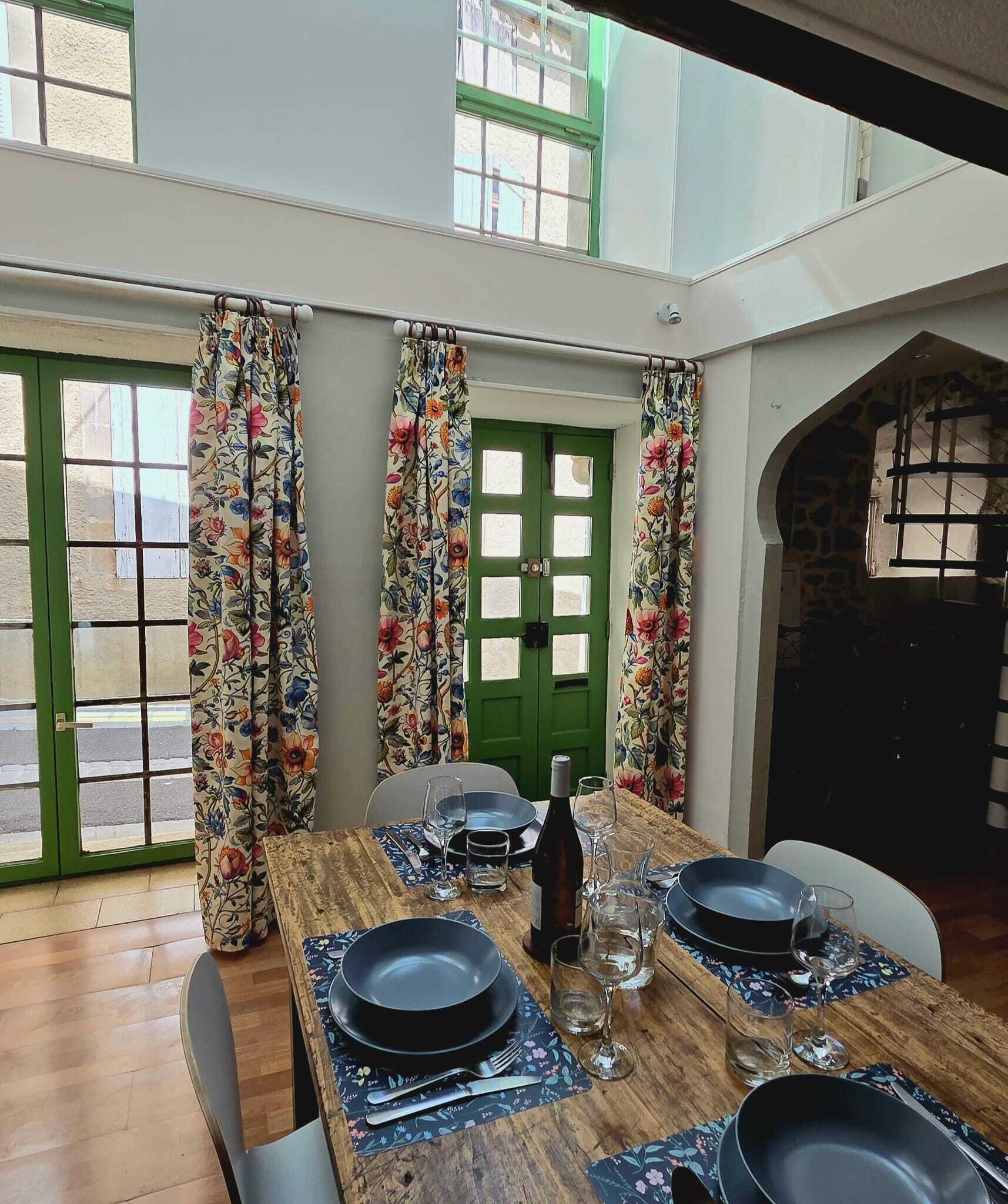 A dining area with a wooden table set for four, a green door, and a view through a window.