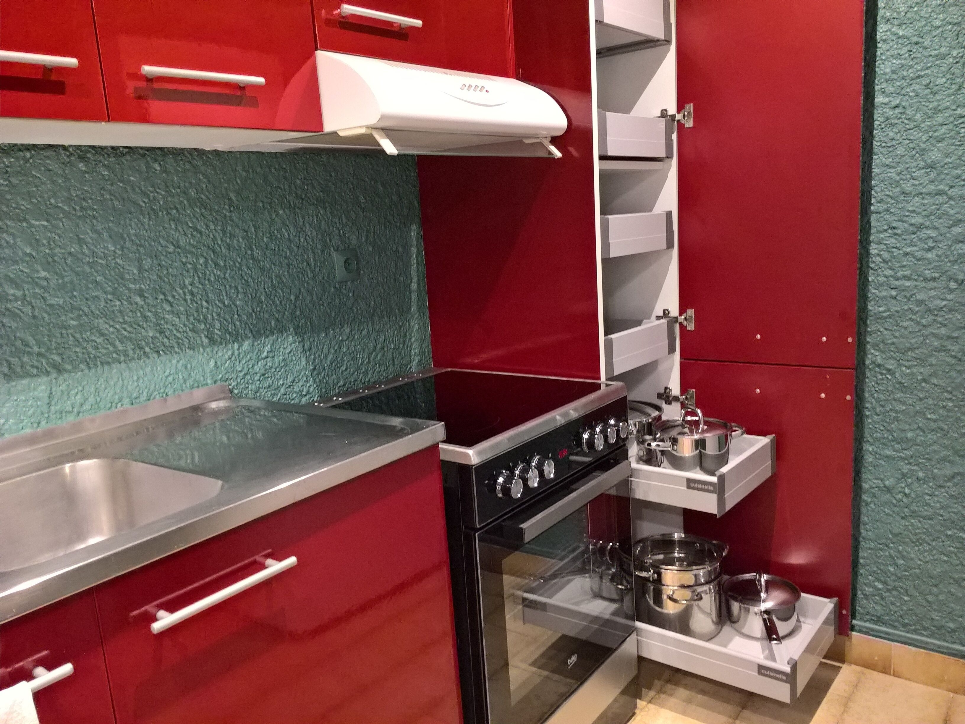 A compact kitchen with red cabinets, a stainless steel countertop, a built-in oven, and a microwave.