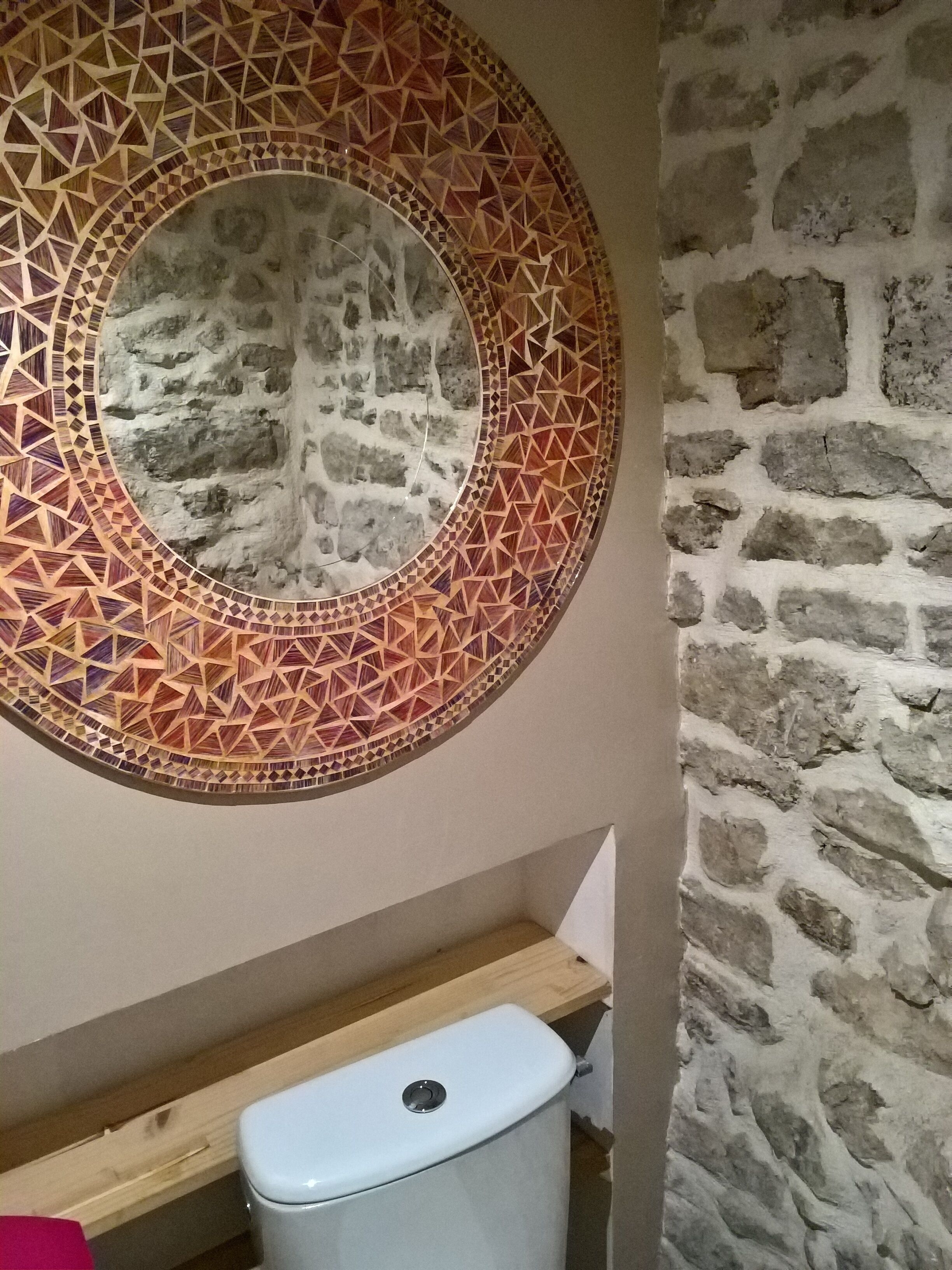 Et badeværelse med en stenvæg, en rund mosaikvæg og et toilet.