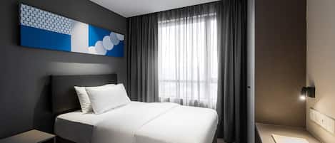 Une chambre d’hôtel moderne avec un grand lit, une table de chevet, un bureau et une fenêtre avec des rideaux.