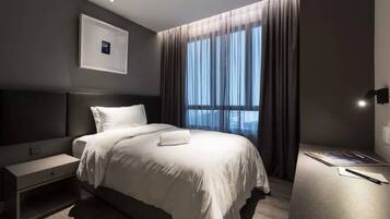Ein modernes Hotelzimmer mit einem großen Bett, einem Nachttisch, einer Lampe an der Wand und einem Fenster mit Vorhängen.