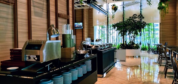 Un hall d’hôtel moderne avec un espace buffet, une machine à café et un écran de télévision.