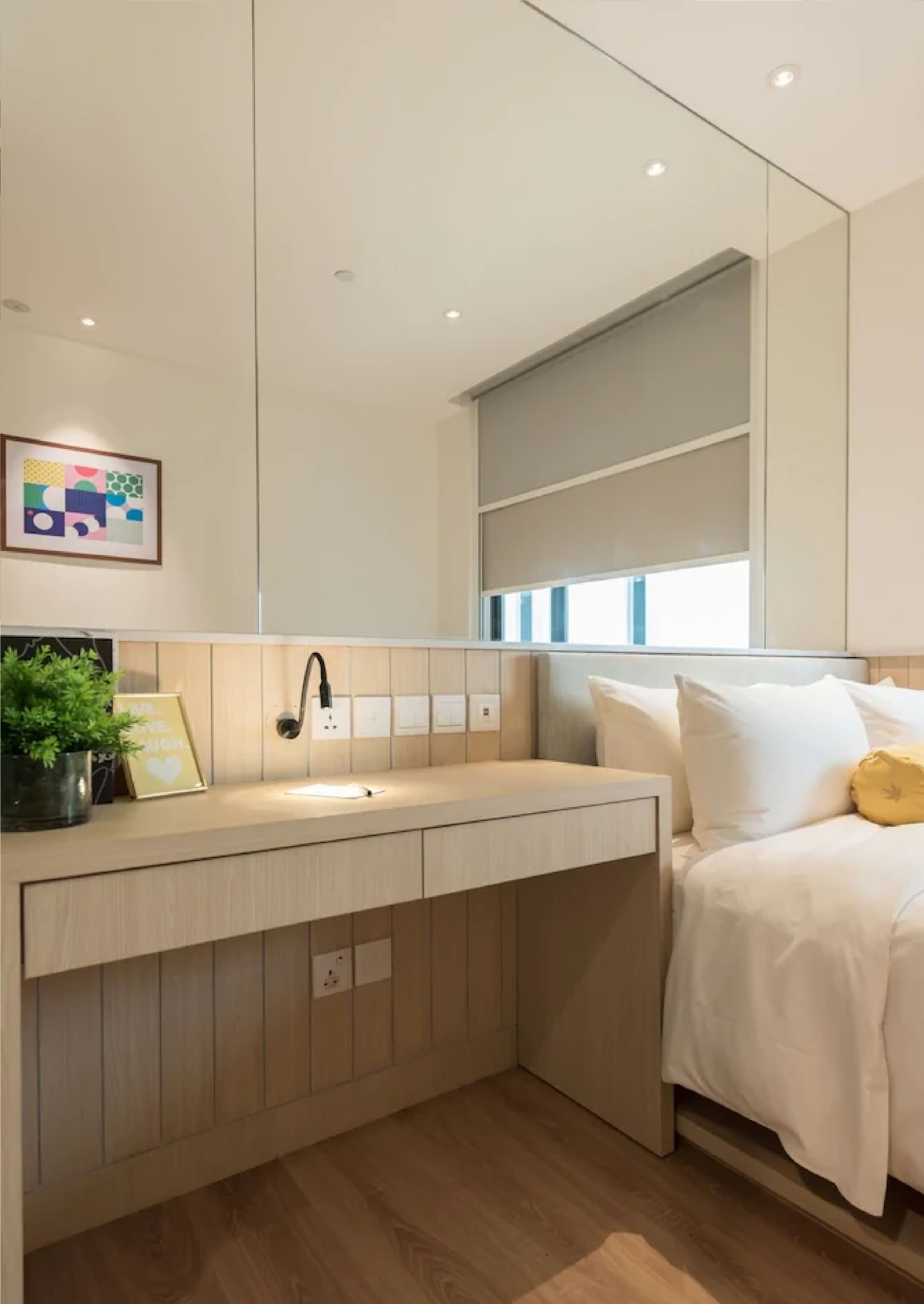 A modern bedroom with a built-in desk, bedside table, and a large mirror.