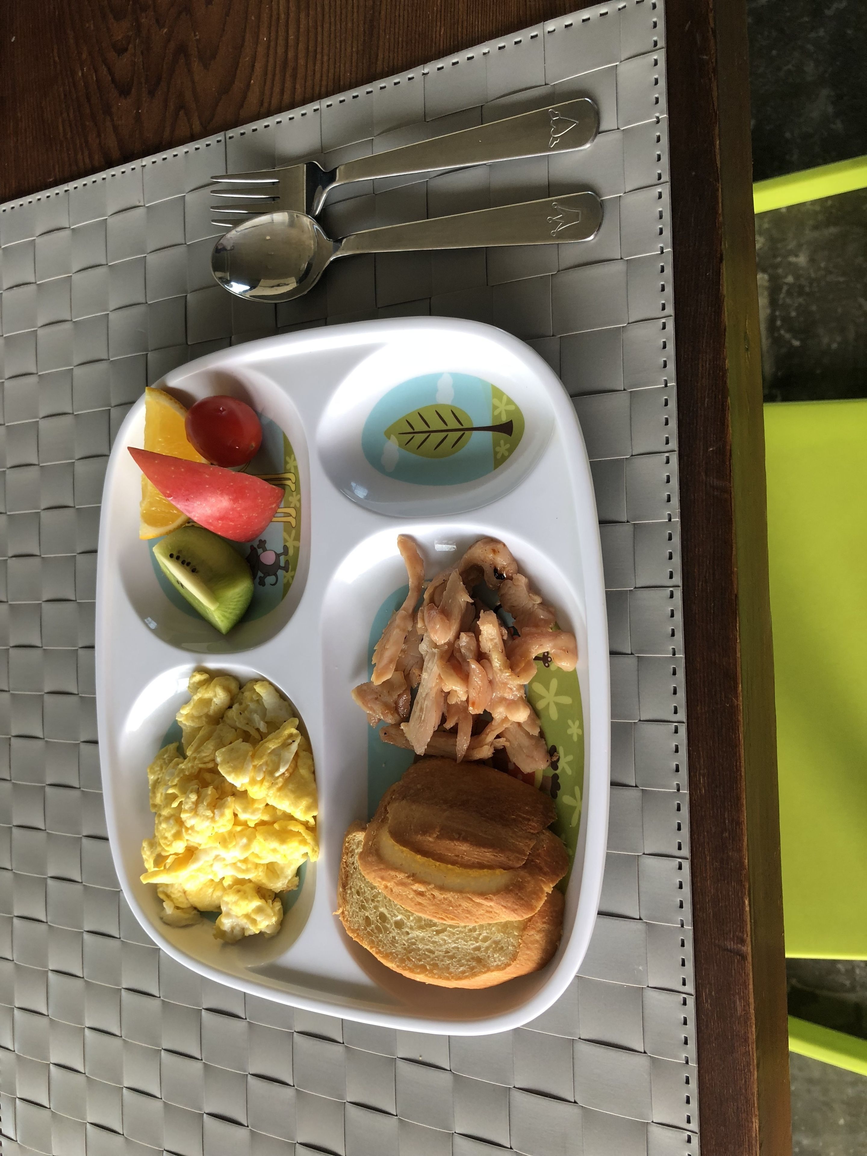 Ein Tablett mit verschiedenen Speisen, darunter Obst, Eier und Fleisch, auf einem Tisch mit einem gemusterten Untersetzer.