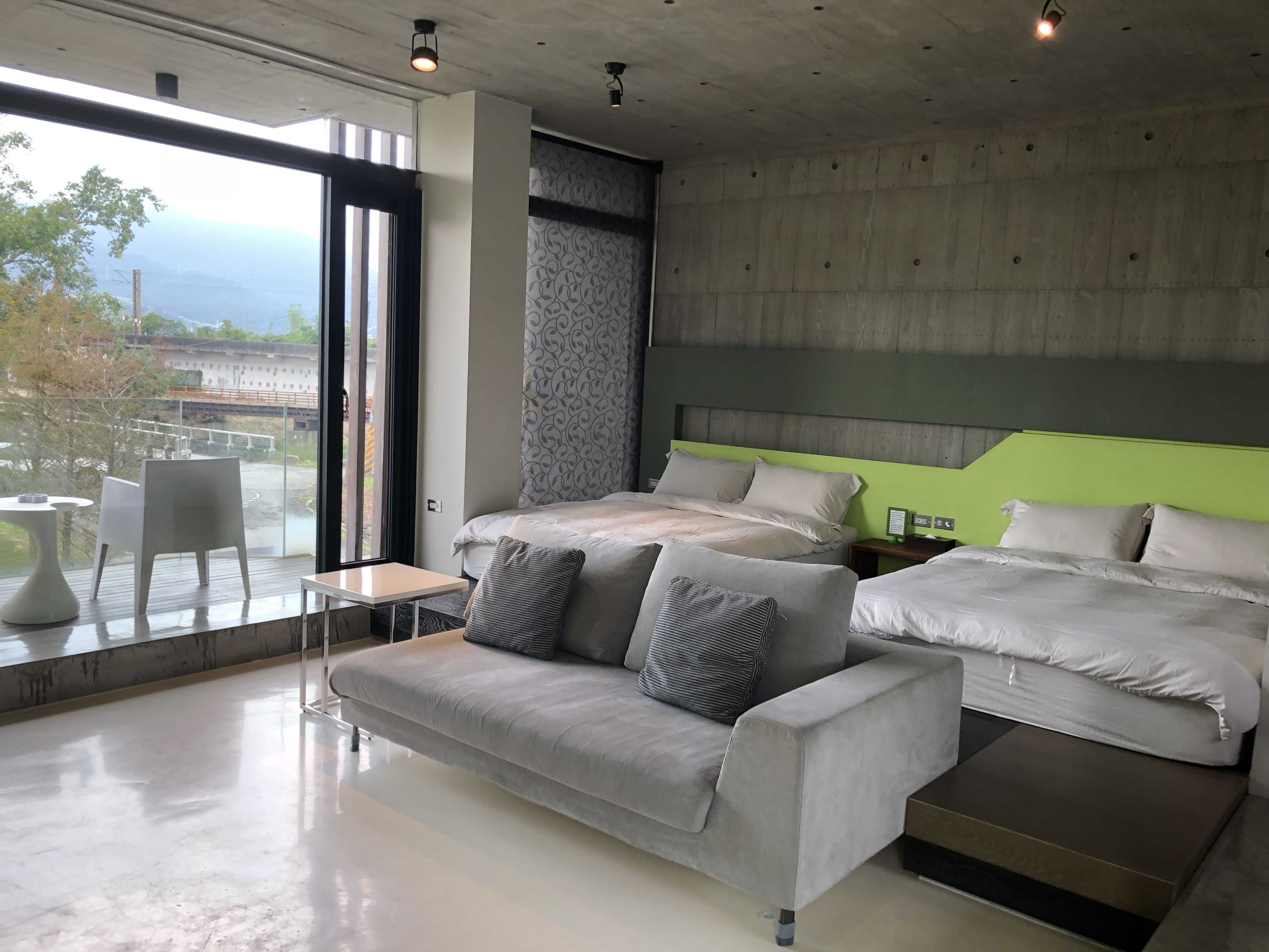Una habitación de hotel moderna con una cama grande, un sofá y un balcón con vistas a un puente.