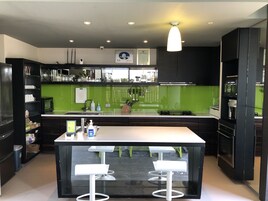 Una cocina moderna con una isla central, taburetes de bar y un salpicadero verde.