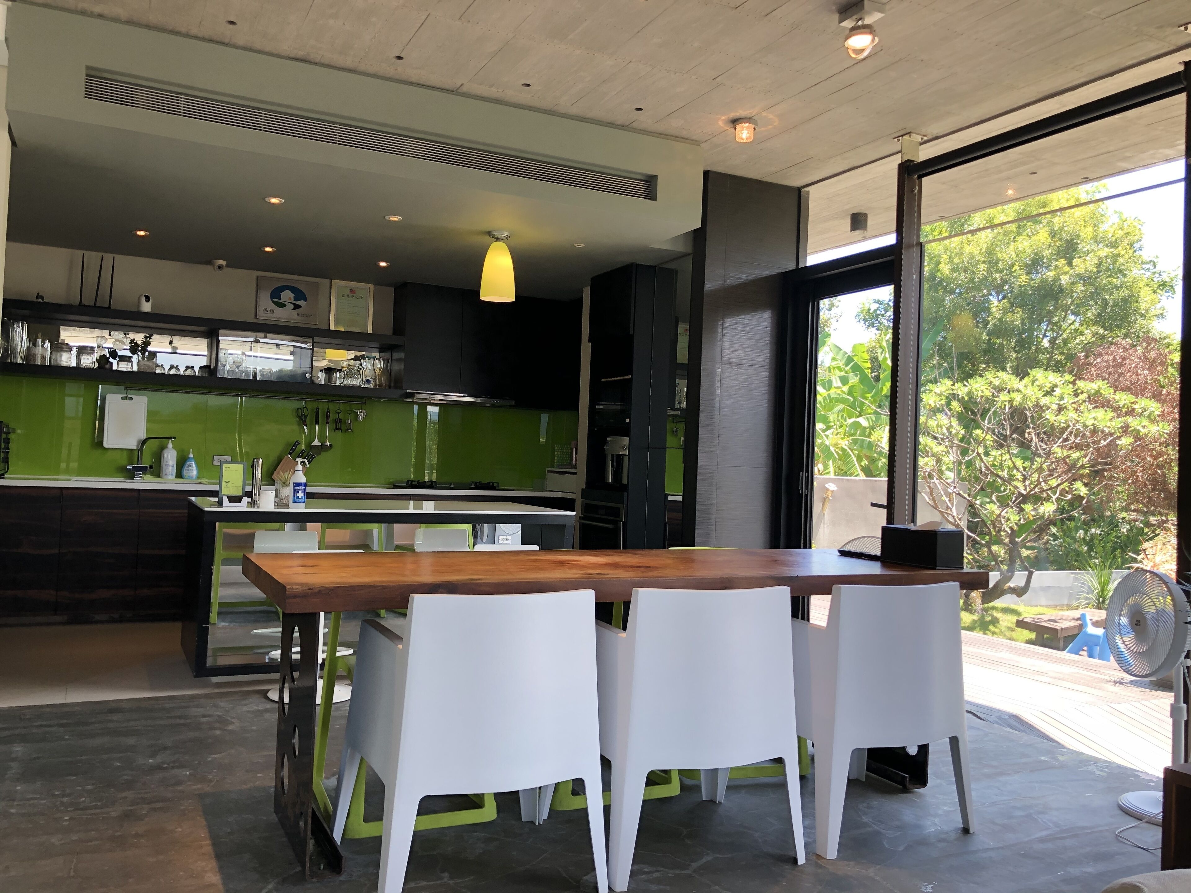 Una cocina moderna con una mesa de comedor de madera y sillas blancas, un salpicadero verde y vistas al exterior.
