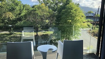 Ein Balkon mit zwei weißen Stühlen und einem kleinen Tisch, mit Blick auf eine Straße und Grünflächen.