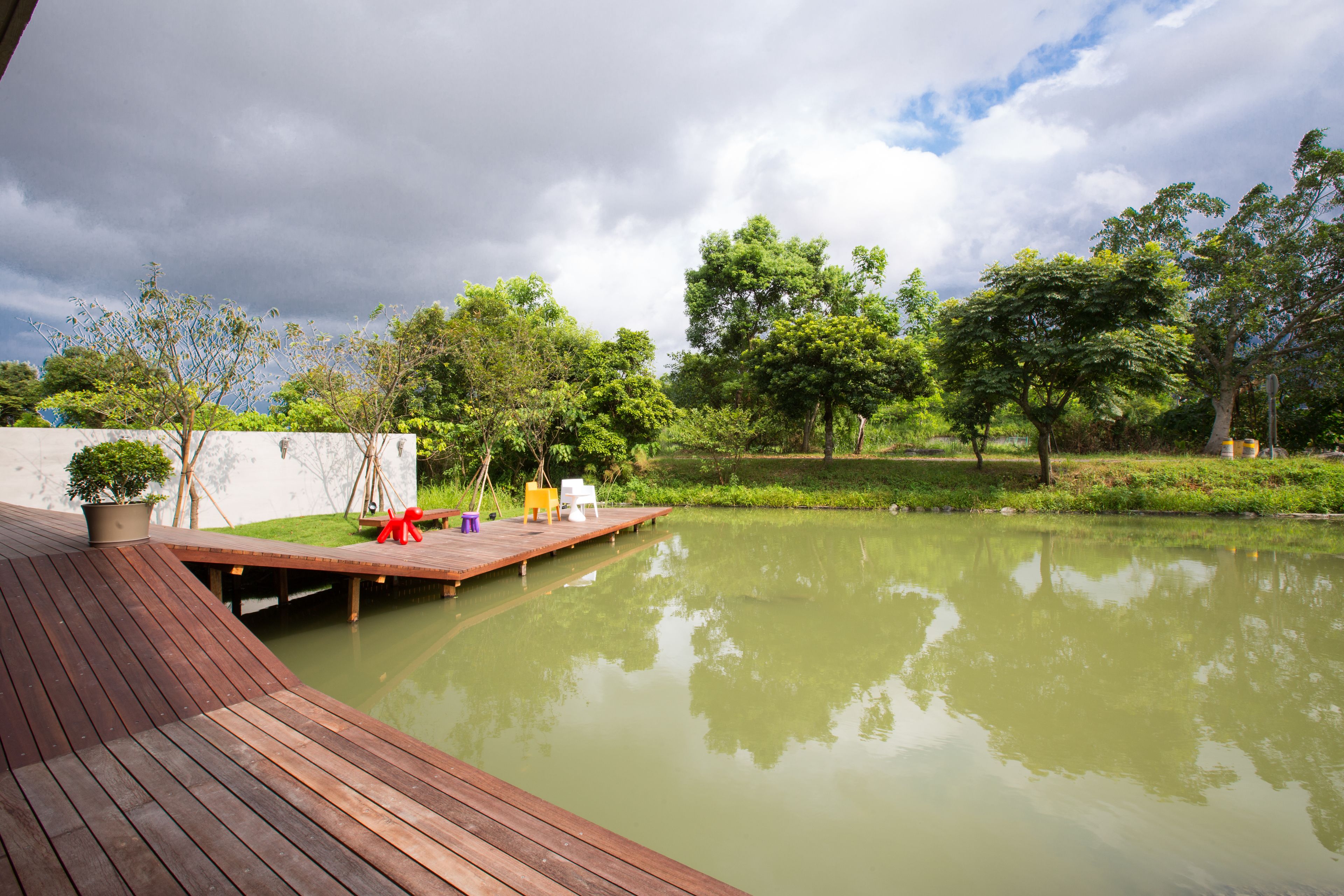 Une terrasse en bois s’étendant au-dessus d’un étang paisible, entourée d’une végétation luxuriante et d’arbres.