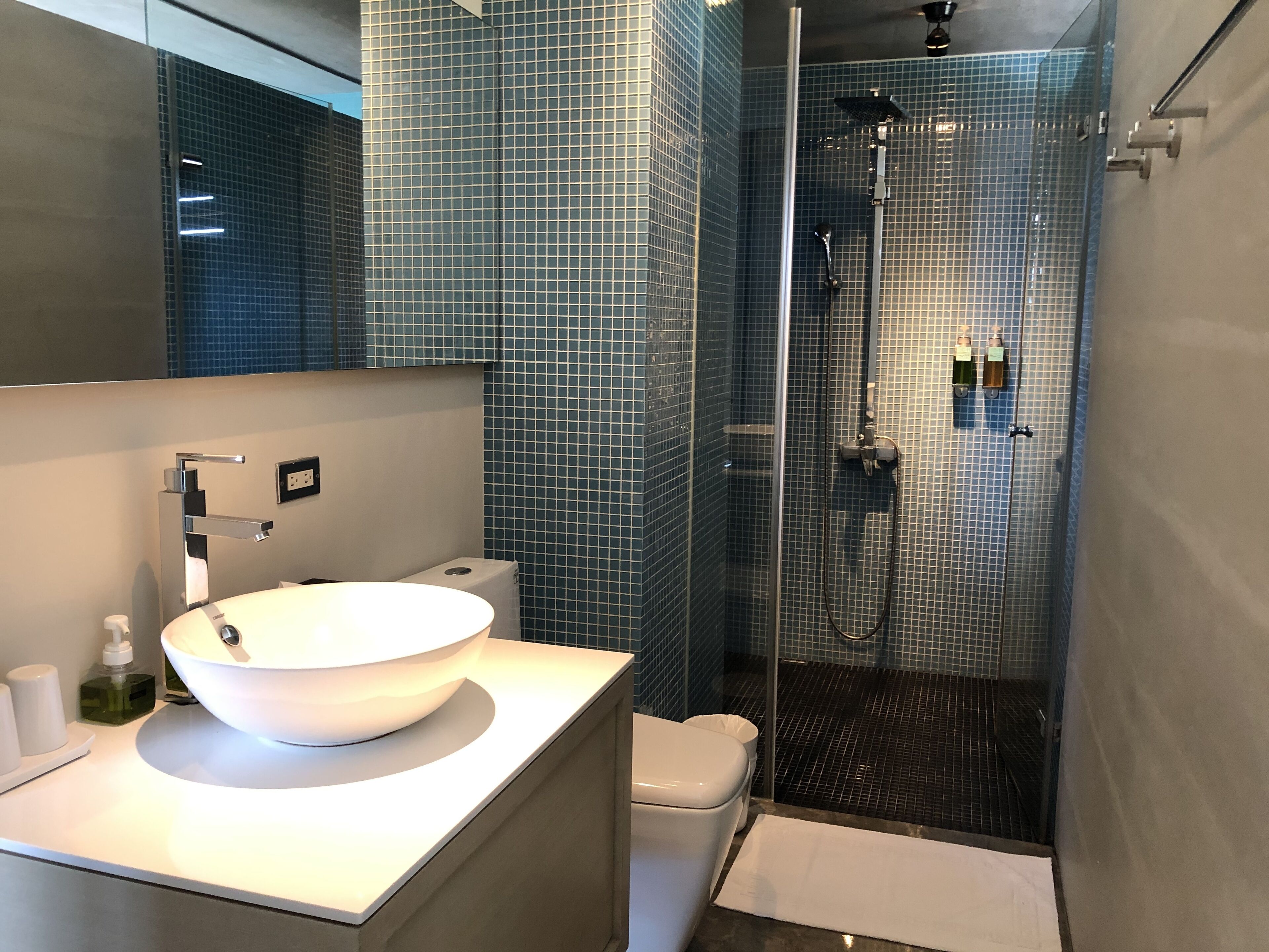 A modern bathroom with a large white sink, a glass-enclosed shower, and a toilet.
