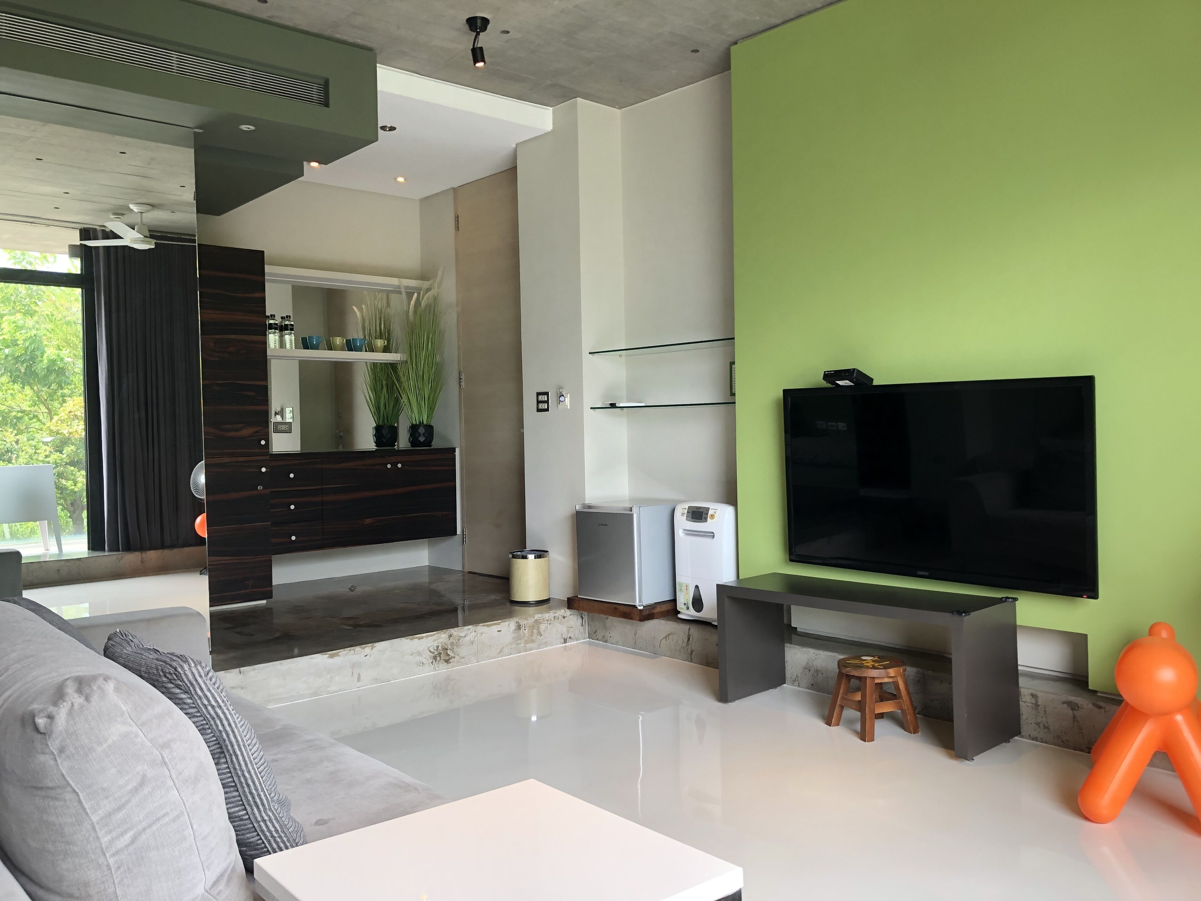 A modern living room with a large flat-screen TV, a grey sofa, a white coffee table, and a green accent wall.