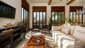 Una sala de estar moderna con sofá, televisión, mesa de centro de madera y ventanas amplias.