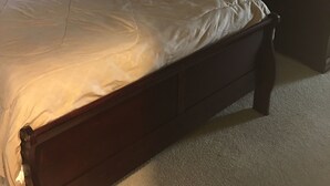 Un lit bien fait, avec une tête de lit en bois, une lampe de chevet et un miroir posé sur une commode.