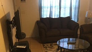 Un salon avec un canapé, une table basse en verre et un téléviseur posé sur un meuble.