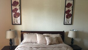 Un lit bien fait, recouvert d’une courtepointe matelassée, deux lampes de chevet et deux tableaux floraux accrochés au mur.
