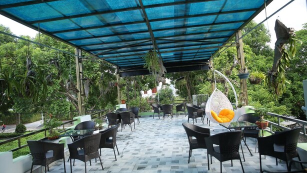 An outdoor patio area with black wicker chairs and tables, a blue canopy, and hanging plants. - TamCoc Green field Hostel (Nam Hoa Lu)