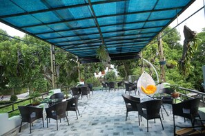 An outdoor patio area with black wicker chairs and tables, a blue canopy, and hanging plants. - TamCoc Green field Hostel (Nam Hoa Lu)