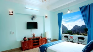 A bedroom with a bed, a TV, a fan, a small table with chairs, and a view of mountains. - TamCoc Green field Hostel (Nam Hoa Lu)
