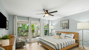 Een slaapkamer met een groot bed, een plafondventilator, een bureau met stoel, een vloerlamp en uitzicht op de omgeving.