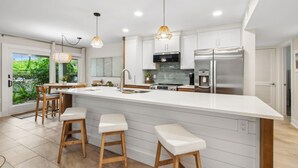 Een moderne keuken met een groot schiereiland, witte kastjes, roestvrijstalen apparatuur en hanglampen.