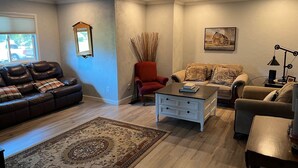 Uma sala de estar com um sofá de couro marrom, uma poltrona vermelha, um sofá bege com almofadas estampadas e um tapete.