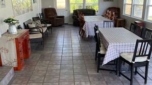 Uma sala de jantar espaçosa com uma mesa grande e cadeiras, um ventilador de teto e vista para o exterior através de amplas janelas.