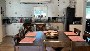 Uma cozinha moderna com armários brancos, uma mesa de jantar com quatro cadeiras e uma ilha central.