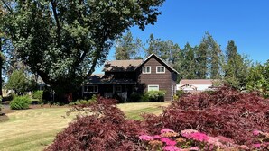 Uma casa de dois andares com fachada marrom escura, varanda frontal e gramado bem cuidado.