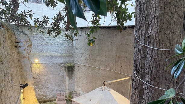 A courtyard with a wooden table and chairs, a hanging umbrella, and potted plants.