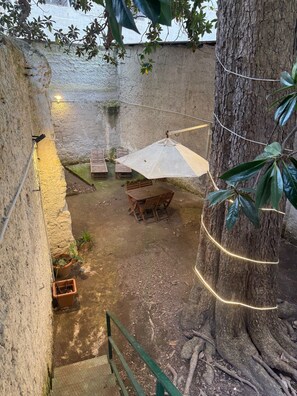 Un cortile con un tavolo e sedie in legno, un ombrellone e piante in vaso.