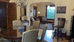 A dining area with a glass table, upholstered chairs, a chandelier, and a view of the outdoors through a window. - Charming Hilltop Home with City View (Chippewa Falls)