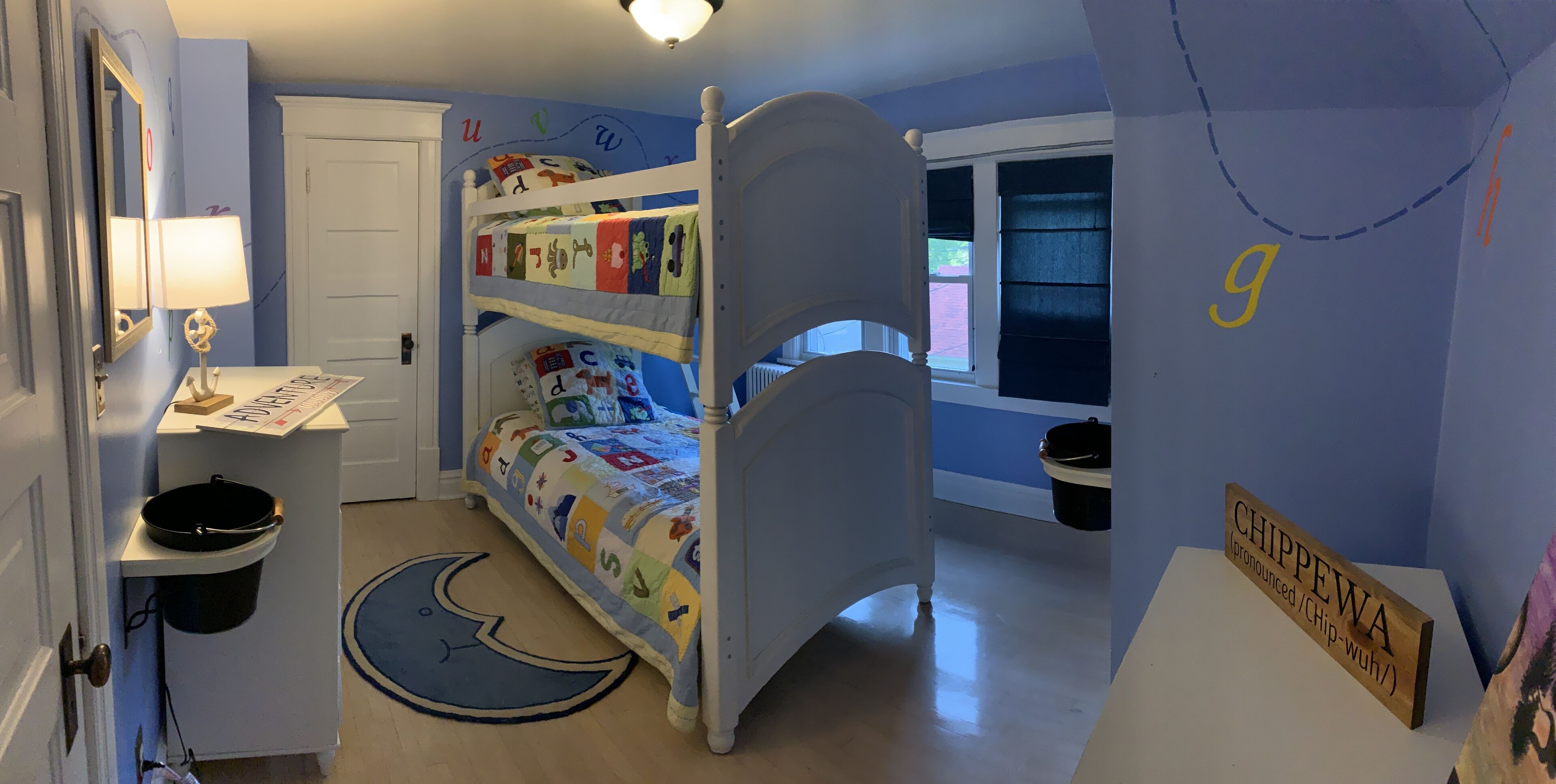 Une chambre d’enfant avec des lits superposés, un bureau et une table de chevet.