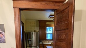 A wooden door leading to a kitchen with a refrigerator, a window, and a dining area. - Charming Hilltop Home with City View (Chippewa Falls)