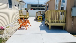 Un étroit sentier mène à une terrasse en bois où se trouvent un banc et des chaises.