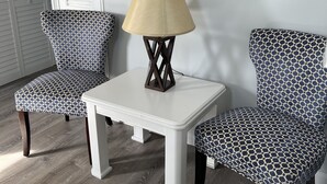 Une pièce comprenant deux fauteuils à motifs, une petite table blanche avec une lampe et trois œuvres d’art murales.