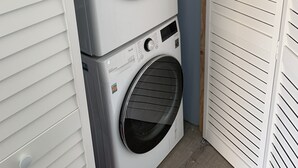 Une machine à laver et un sèche-linge superposés dans une buanderie aux murs blancs et au plancher en bois.