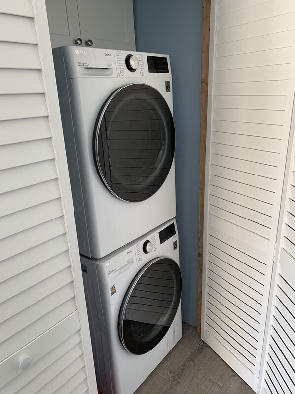 Une machine à laver et un sèche-linge superposés dans une buanderie aux murs blancs et au plancher en bois.