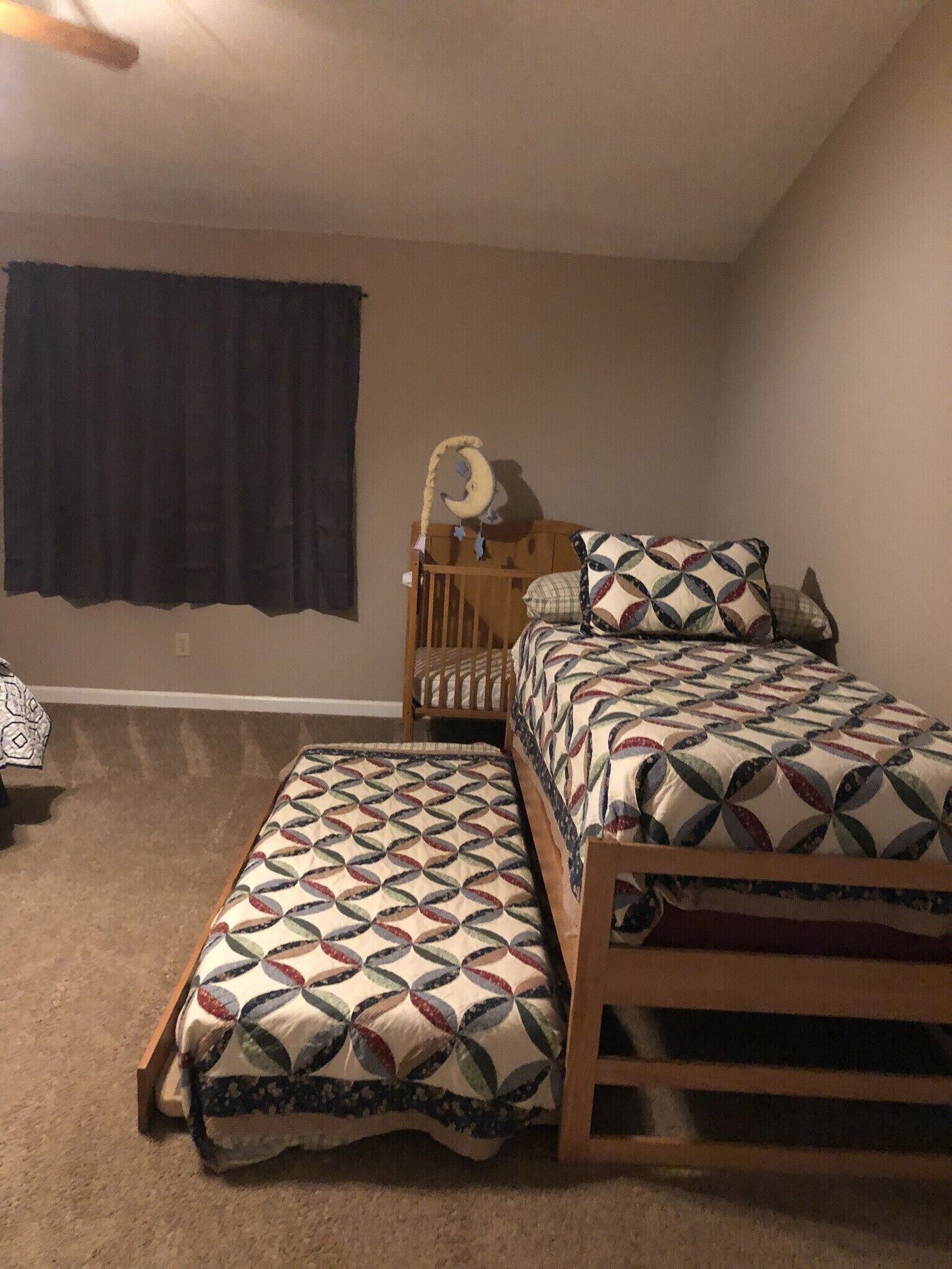 A bedroom with a single bed, a nightstand, a crib, and a window with dark curtains.