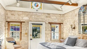 Una habitación rústica con paredes de piedra, una cama, una silla y una puerta con vidrieras.