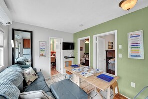 Un salon moderne avec un canapé, une table à manger et un coin cuisine visible à travers une porte ouverte.