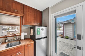 A kitchen with wooden cabinets, a stainless steel sink, a refrigerator, and a window overlooking a street. - WildWoof Beach Bungalow @ North Wildwood - No Pet Fees! (North Wildwood)