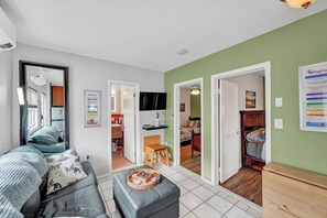 Un salon comprenant un canapé, un pouf et une petite table avec un plateau. Des portes donnent accès aux autres pièces.