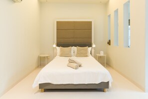A neatly made bed with a white bedspread and beige pillows, a bedside table with a lamp, and a wall-mounted mirror. - Parkview at KLCC (Kuala Lumpur)