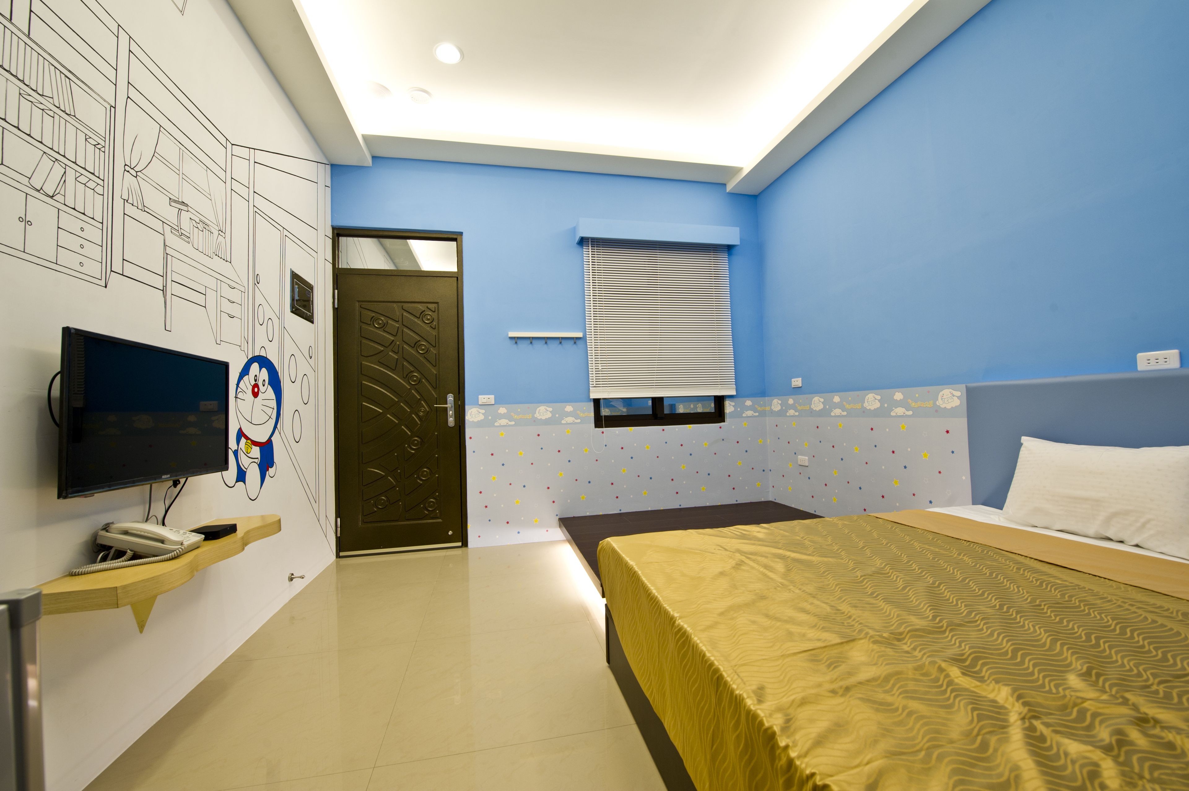 A hotel room with a bed, a desk with a telephone, a TV, and a door.