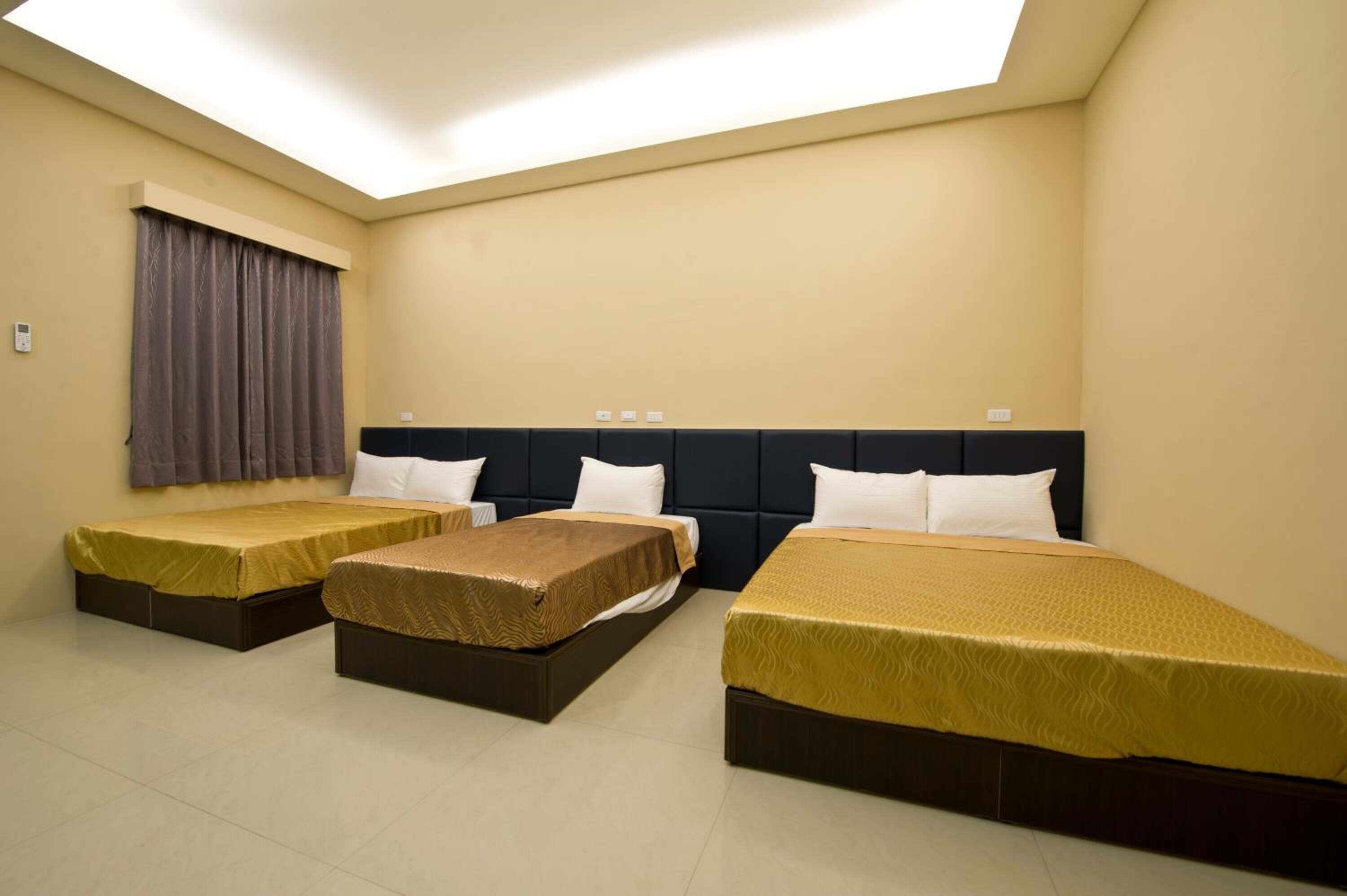 Habitación de hotel con tres camas individuales, un ventanal con cortinas y una lámpara en el techo.